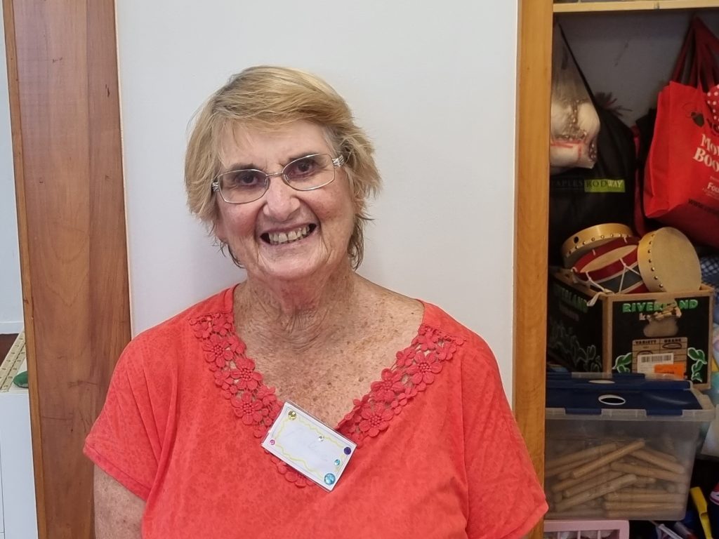 Woman wearing red top. Smiling. Toys visible in the background.