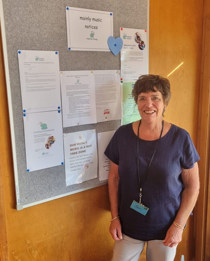 Woman smiling, standing in front of a noticeboard all about 'mainly music.'