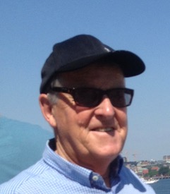 Man, who is smiling, wearing sunglasses and a cap outdoors.