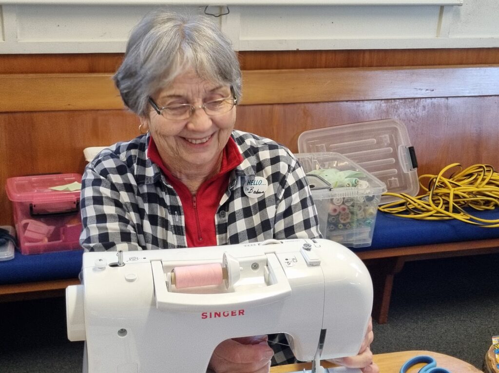 Woman at a sewing machine. She is smiling. Cables and supplies in the background.