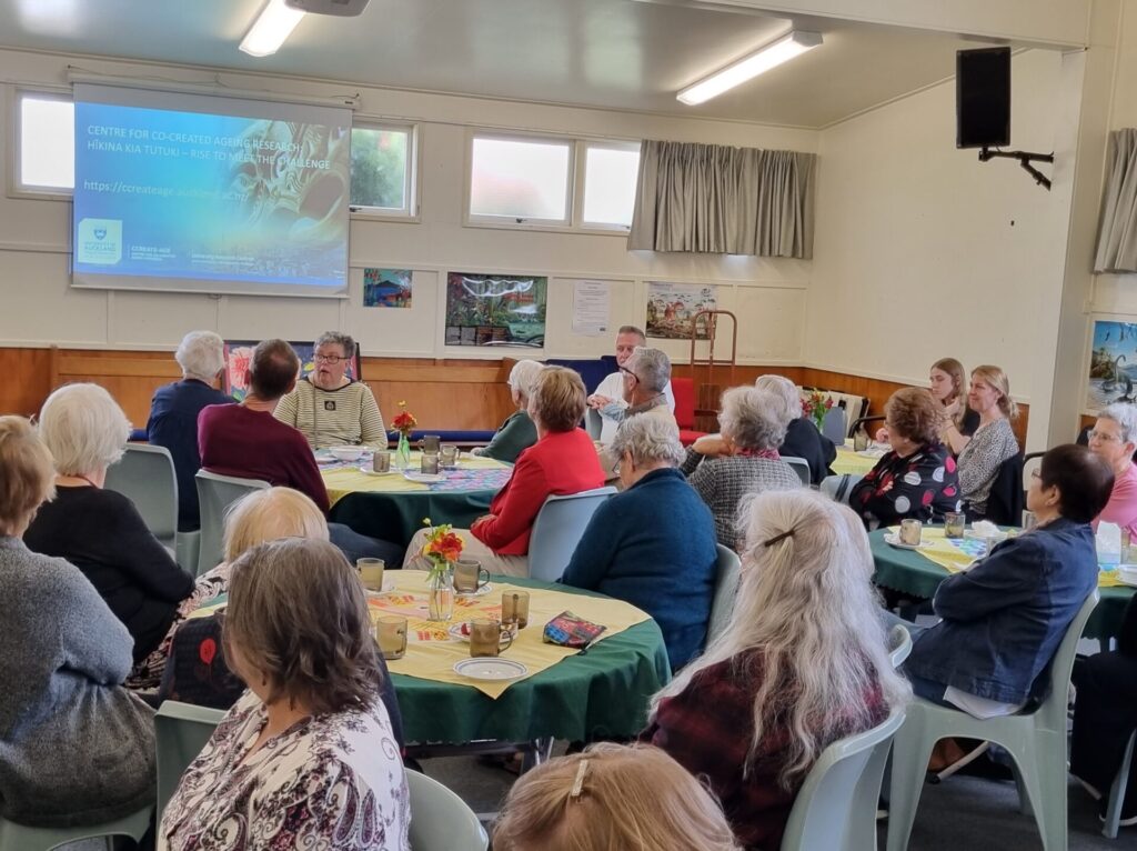 Tables of people in the hall looking at a PowerPoint presentation on ageing research.