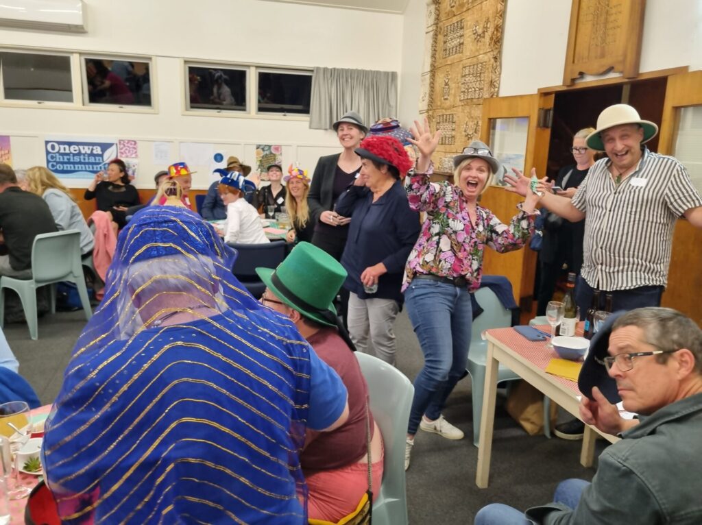 Guests in the hall wearing a variety of hats. A couple pose for the camera: 'cheers!'