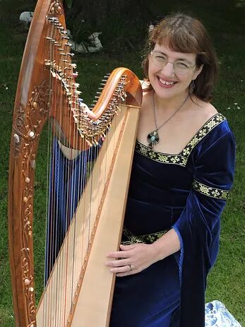 A woman in a long velvet gown is holding her harp; she is smiling at the camera.